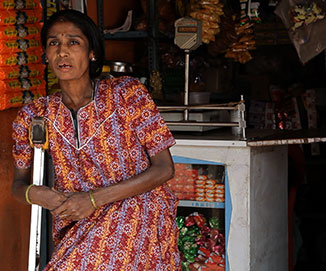 Woman with crutches standing in front of kirana shop